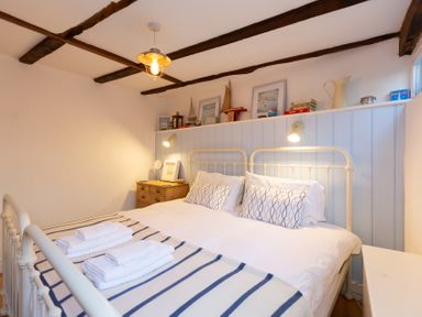 A bedroom with a double bed with white and blue striped bedding and two side tables with lamps at The Sail Loft in St Ives