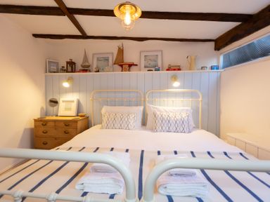 A bedroom with a double bed two pillows bedside table with a mirror and decorations on a shelf at The Sail Loft in St Ives