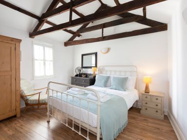 A bedroom with a bed two light blue pillows a wooden wardrobe a wooden chair a black dresser with a mirror and two lamps at The Sail Loft in St Ives