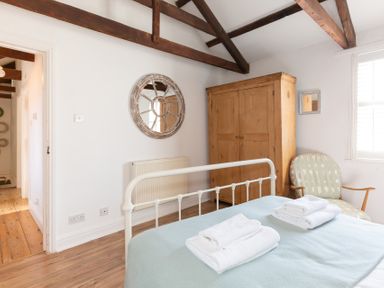 A bedroom with a metal bed frame folded towels a wooden wardrobe a chair and a round wall mirror at The Sail Loft in St Ives