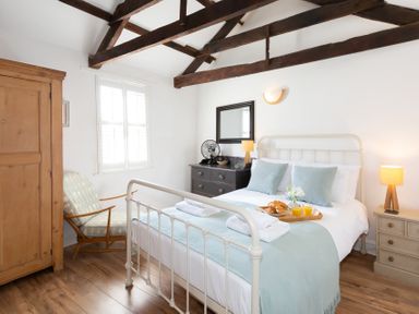 A bedroom with a white metal bed frame two bedside tables with lamps a wooden wardrobe and a cushioned chair at The Sail Loft in St Ives
