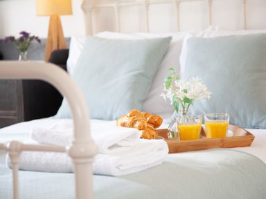 A bed with two pillows towels croissants orange juice and a flower vase at The Sail Loft in St Ives