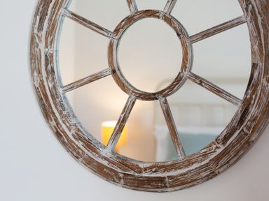 A close up of a round wooden mirror reflecting a lamp and part of a bed at The Sail Loft in St Ives