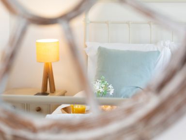 A bedroom with a bed holding a blue pillow and white flowers with a wooden lamp on a bedside table at The Sail Loft in St Ives