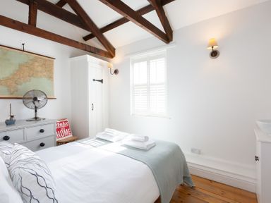 A bedroom with a bed folded towels wooden floor and white walls at The Sail Loft in St Ives