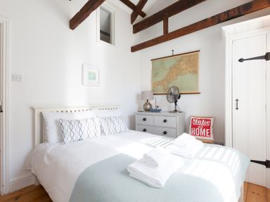 A bedroom with a bed folded towels and a chest of drawers with a fan and lamp at The Sail Loft in St Ives