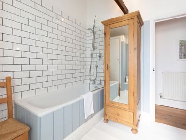 A bathroom with a bathtub shower and a wooden armoire with a mirror at The Sail Loft in St Ives