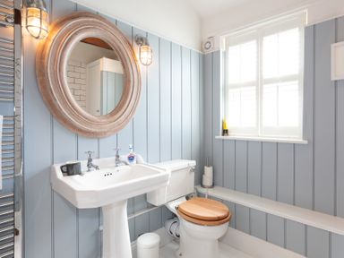 A bathroom with a pedestal sink and toilet with wooden seat next to a window at The Sail Loft in St Ives