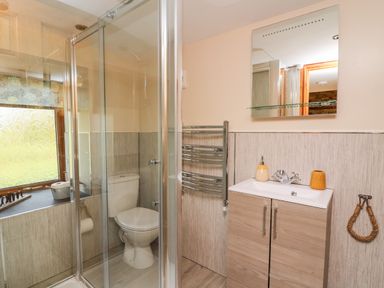 A bathroom with a shower enclosure, toilet, sink with cabinet, mirror, and towel racks at Tegfan Barn in Pant-y-dwr near Rhayader