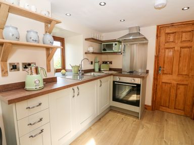 A kitchen with wooden countertops white cabinets a stainless steel oven and hood a green kettle and toaster at Tegfan Barn Pant-y-dwr near Rhayader