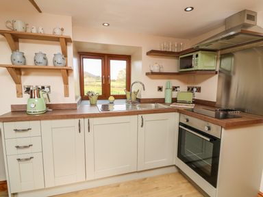 A kitchen with wooden shelves and countertop a window above the sink and an oven with a microwave at Tegfan Barn Pant-y-dwr near Rhayader