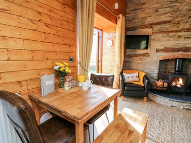 A wooden dining table with chairs and flowers next to a stone wall with a fireplace and armchair at Tegfan Barn Pant-y-dwr near Rhayader