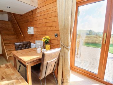 A wooden dining area with a table and leather chairs next to a glass door with a view of a fenced yard at Tegfan Barn in Pant-y-dwr near Rhayader