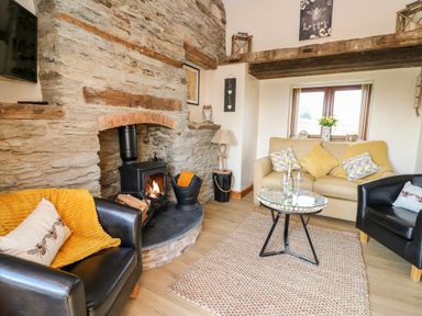 A living room with a stone fireplace a wood-burning stove sofa armchairs and a glass coffee table at Tegfan Barn Pant-y-dwr near Rhayader