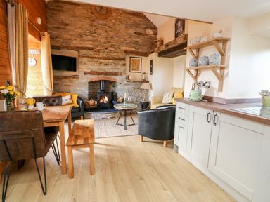 A kitchen and living area with wooden dining table chairs wood burning stove and shelves with jars at Tegfan Barn in Pant-y-dwr near Rhayader