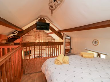 A loft bedroom with a bed and rolled towels wooden beams and a TV at Tegfan Barn Pant-y-dwr near Rhayader