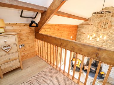 A wooden loft area with a chest of drawers a hanging rail with hangers and a view over a living room with a fireplace at Tegfan Barn Pant-y-dwr near Rhayader