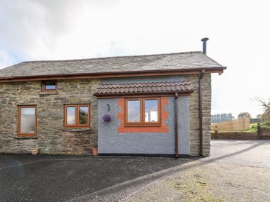 The exterior of a stone and brick house with three windows a tiled roof and a paved driveway at Tegfan Barn Pant-y-dwr near Rhayader