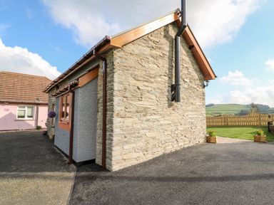 An outdoor area with a stone and gray building and a fenced grassy yard at Tegfan Barn Pant-y-dwr near Rhayader