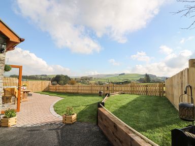 A fenced backyard with a paved patio area and grassy lawn at Tegfan Barn in Pant-y-dwr near Rhayader