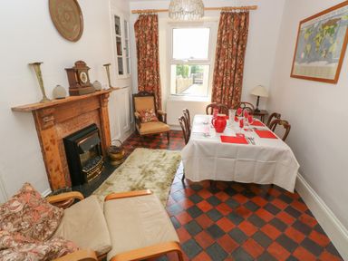 A dining room with a fireplace armchairs a table set with red placemats and glasses and a window with patterned curtains at Hawthorn House in Pembroke