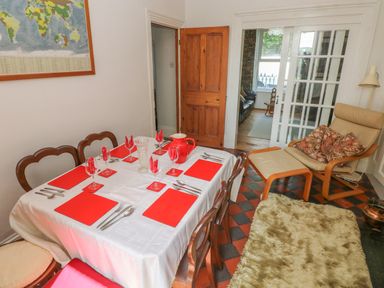 A dining room with a table set with red placemats and napkins beside a lounge chair with cushions at Hawthorn House in Pembroke