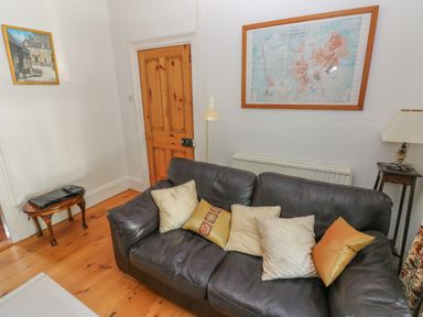 A room with a leather sofa with cushions a wooden door a small wooden table with electronic devices and framed pictures on the walls at Hawthorn House in Pembroke