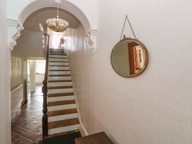 A staircase with wooden steps and white risers under an archway with a pendant light and a round mirror hanging on the wall at Hawthorn House in Pembroke