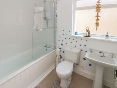 A bathroom with a bathtub shower combo a toilet and a sink with blue polka dots on the wall at Hawthorn House in Pembroke