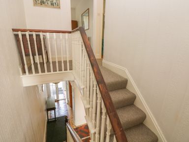 A staircase with beige carpet and white banister leading down to a tiled hallway with a wooden table at Hawthorn House in Pembroke