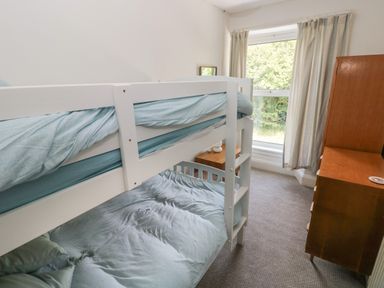 A bedroom with bunk beds a wooden dresser a bedside table with lamp and a window with curtains at Hawthorn House in Pembroke