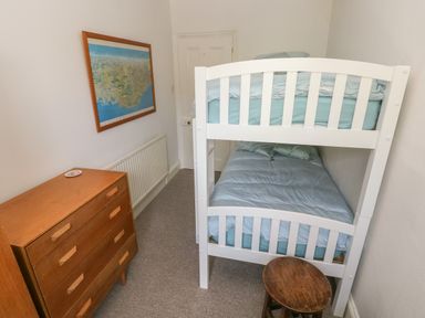 A narrow bedroom with white bunk beds a wooden chest of drawers a small round wooden stool and a framed map on the wall at Hawthorn House in Pembroke