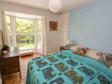 A bedroom with a bed with elephant patterned bedding beside a bay window and wooden chest at Hawthorn House in Pembroke