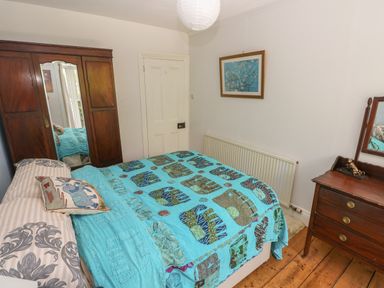 A bedroom with a bed covered by a patterned blanket a wooden wardrobe a wooden dresser and a framed picture on the wall at Hawthorn House in Pembroke