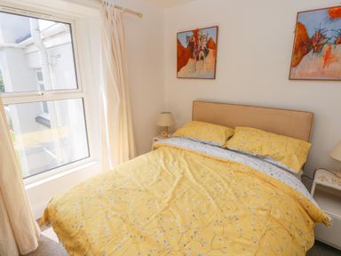 A bedroom with a double bed with yellow floral bedding two bedside tables with lamps and two abstract paintings on the wall at Hawthorn House in Pembroke