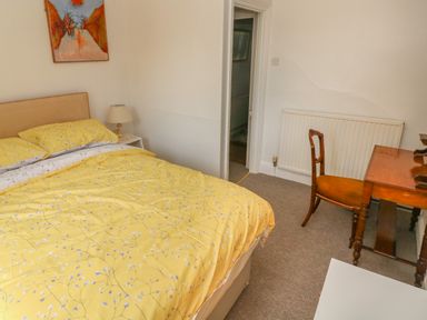 A bedroom with a bed with yellow floral bedding a wooden desk and chair a bedside table with a lamp a radiator and a doorway at Hawthorn House in Pembroke