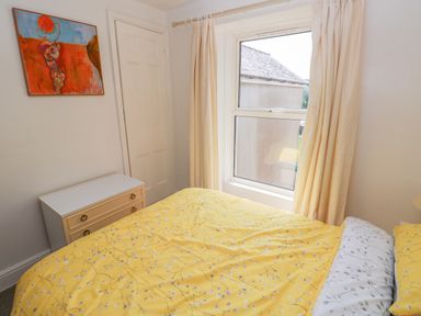 A bedroom with yellow floral bedspread a white chest of drawers and a window with cream curtains at Hawthorn House in Pembroke
