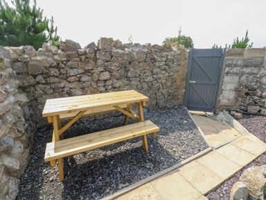 An outdoor area with a wooden picnic table gravel ground stone walls and a blue gate at Hawthorn House in Pembroke