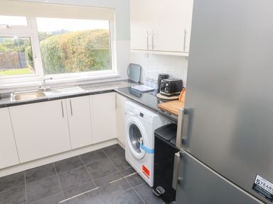 A kitchen with a sink washing machine toaster and refrigerator with view of garden through window