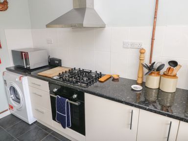 A kitchen countertop with a washing machine microwave cutting board gas stove oven and utensils at Hawthorn House in Pembroke