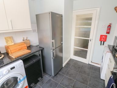A kitchen with a silver refrigerator washing machine black trash bins wooden bread box and a door with frosted glass at Hawthorn House in Pembroke