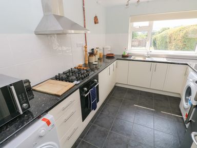 A kitchen with white cabinets black countertops a gas stove a microwave a washing machine and a window overlooking greenery at Hawthorn House in Pembroke