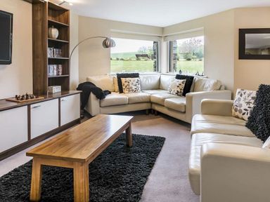 A living room with a wooden coffee table a black rug white sofas and large windows at The Golf Apartment in Kendal