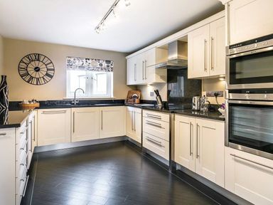 A kitchen with white cabinets black countertops stainless steel appliances and a wall clock at The Golf Apartment in Kendal