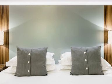 A bed with two gray pillows and white sheets against a light-colored wall with wooden accents and wall lamps at The Golf Apartment in Kendal
