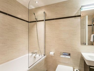 A bathroom with a bathtub shower combination a sink and a toilet at The Golf Apartment in Kendal
