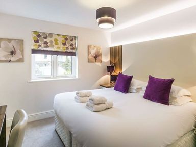 A bedroom with a large bed with white linens and purple pillows at The Golf Apartment in Kendal