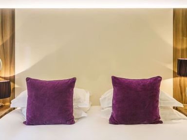 A bed with white pillows and two purple square cushions in a bedroom at The Golf Apartment in Kendal