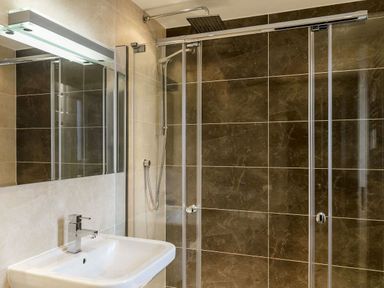 A bathroom with a wall-mounted sink and a shower with glass doors and a rainfall showerhead at The Golf Apartment in Kendal