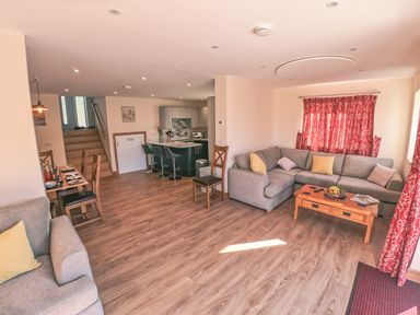 An open living room and kitchen with grey sofas and a wooden coffee table at Swallows Dip in Honiton